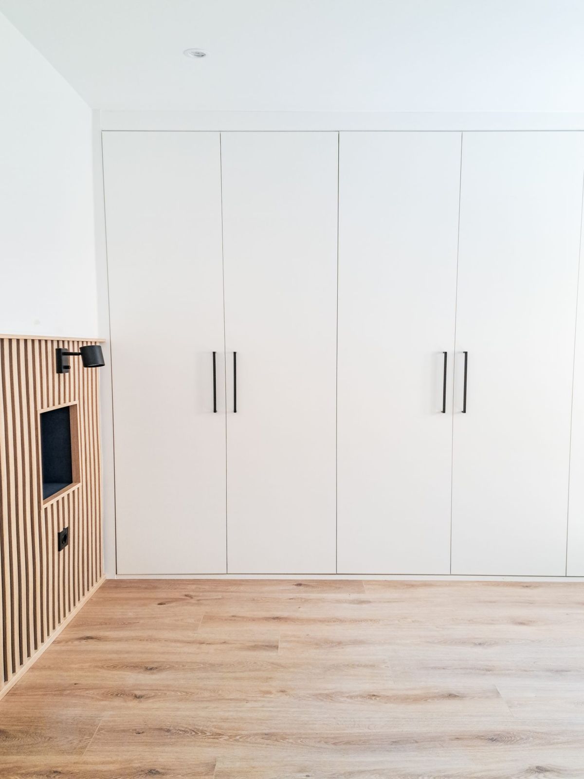 Dormitorio con armarios blancos de pared a pared y cabecero de listones de roble con hornacina en una reforma integral de 150 m² en Castellana, Madrid