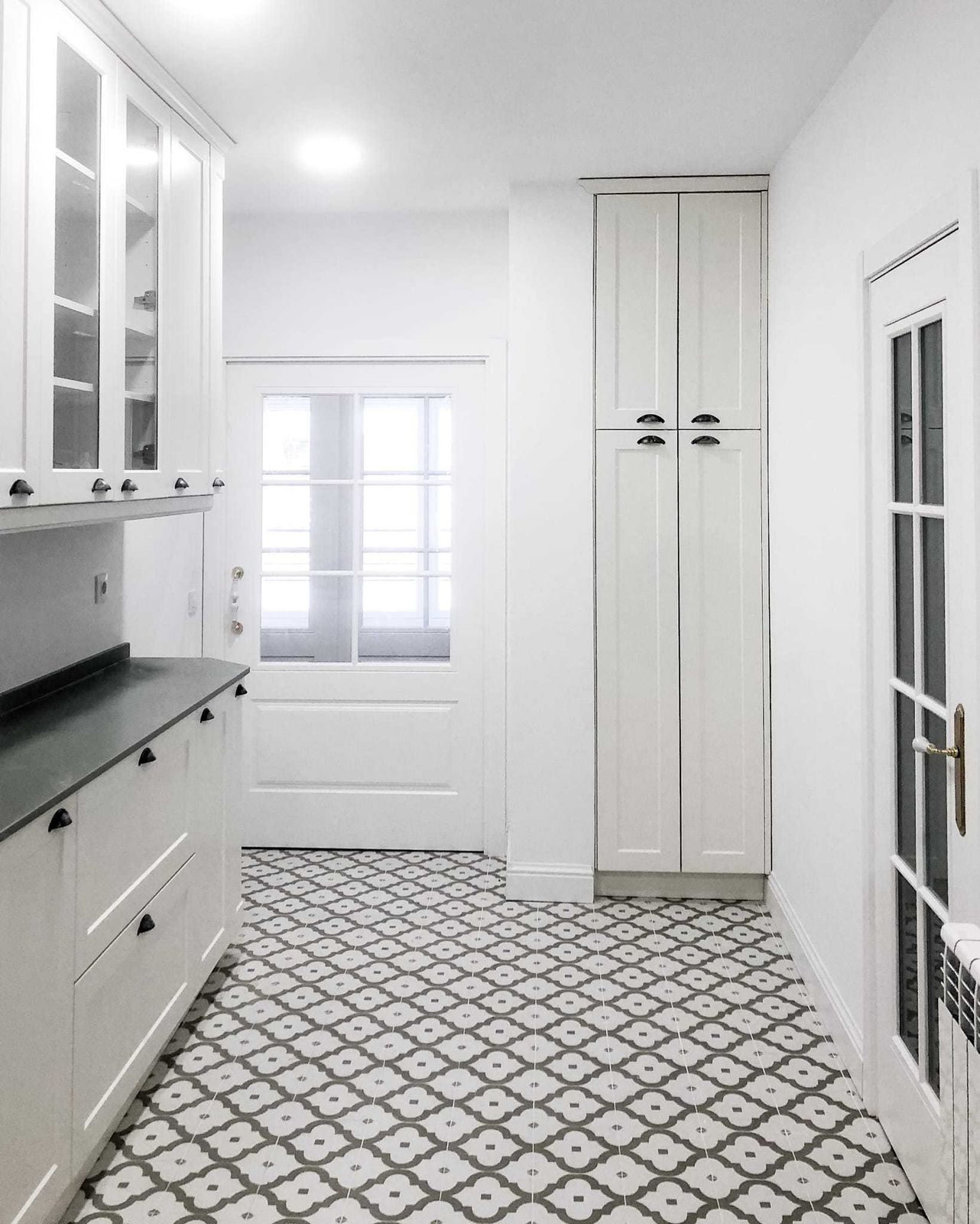Cocina blanca con vitrinas de aire clásico, encimera oscura, armario despensero y suelo hidráulico gris y blanco tras la reforma integral de 120 m² en El Viso, Chamartín