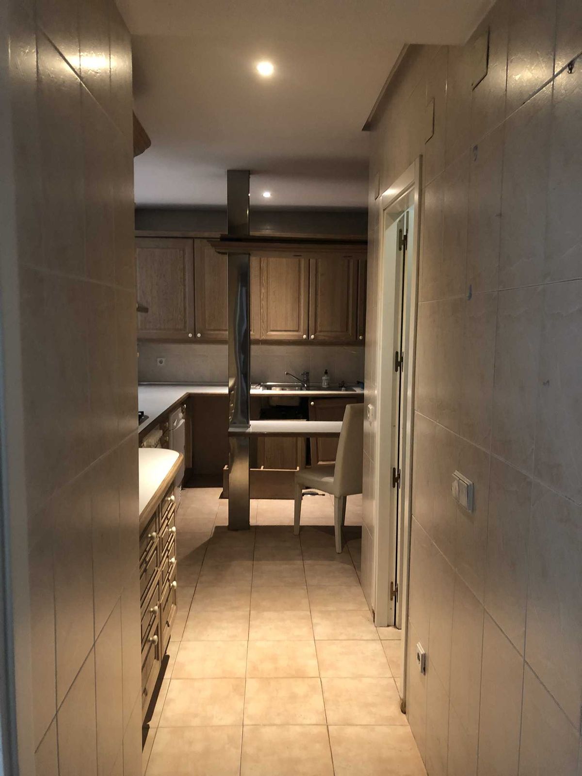 Cocina antes de la reforma integral de 120 m² en El Viso, Chamartín: muebles marrones de los noventa, azulejo beige hasta el techo y un pilar metálico en mitad de la estancia