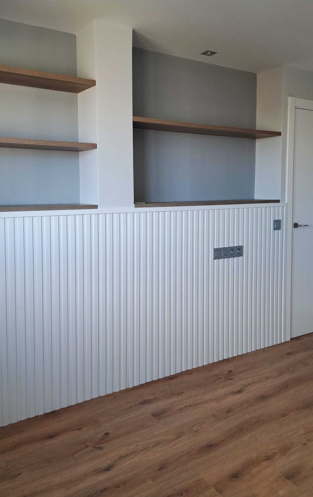 Salón con arrimadero acanalado blanco y baldas de madera sobre pared gris en la reforma integral de una casa de 200 m² en Las Rozas